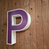 Led letter in paars/wit op houten wand, met kabel onderaan.