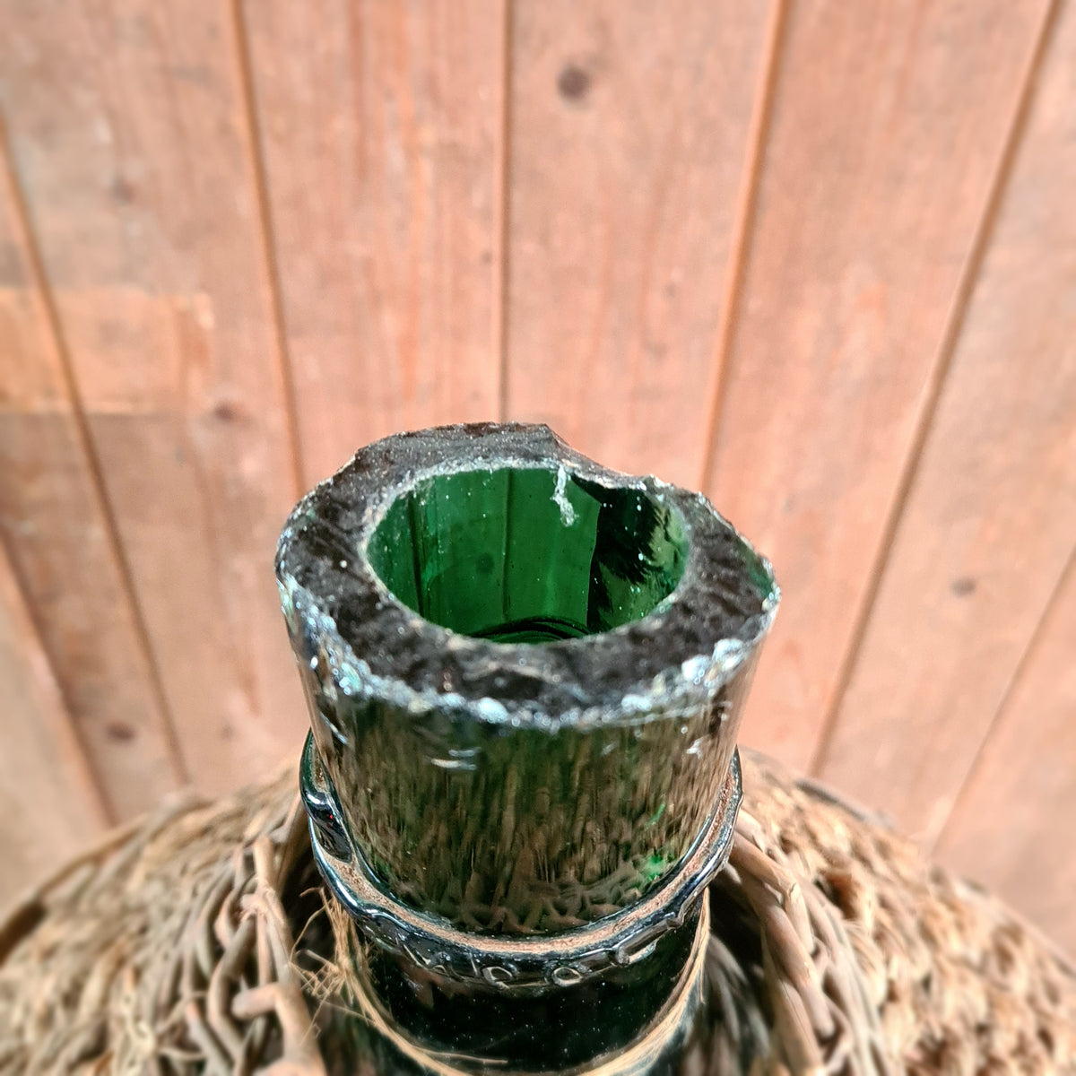 Oude gistfles met gebroken groene glazen hals in mand.