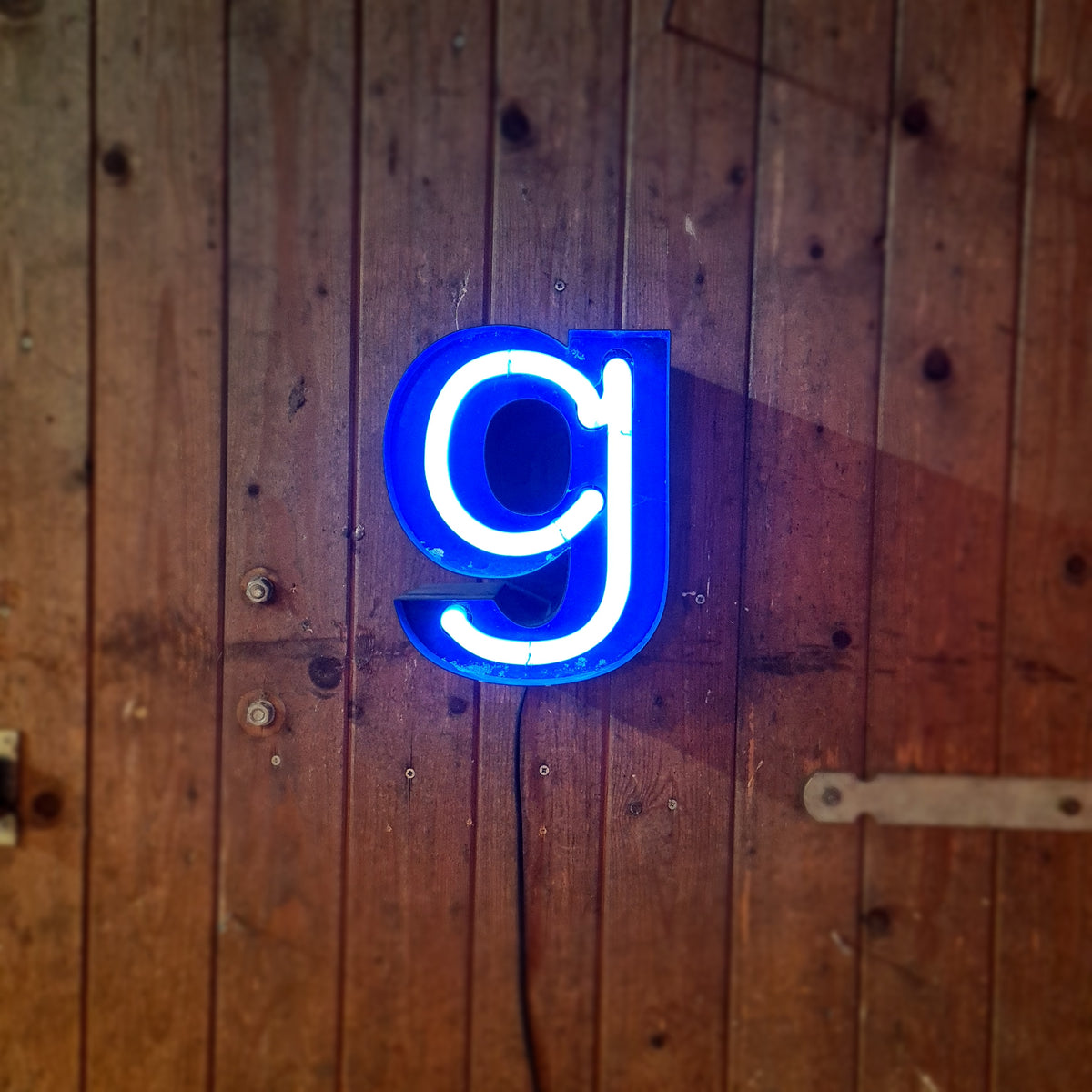 Industriële verlichting: Klein formaat neonletter in blauw op houten wand, rauwe staat. - Heavy Stuff