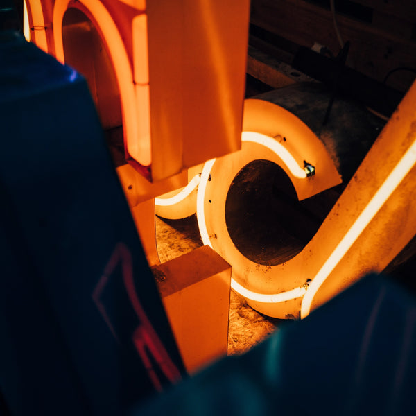 Close-up van reparatie aan vintage neon letters, met een fel oranje-geel verlichte buis in een gedemonteerde metalen letterbehuizing, tonend het vakmanschap van neonrestauratie.