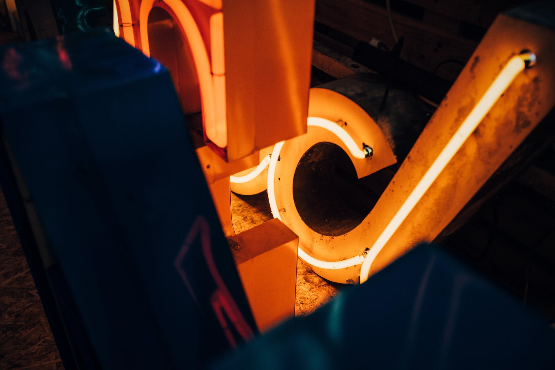 Close-up van reparatie aan vintage neon letters, met een fel oranje-geel verlichte buis in een gedemonteerde metalen letterbehuizing, tonend het vakmanschap van neonrestauratie.