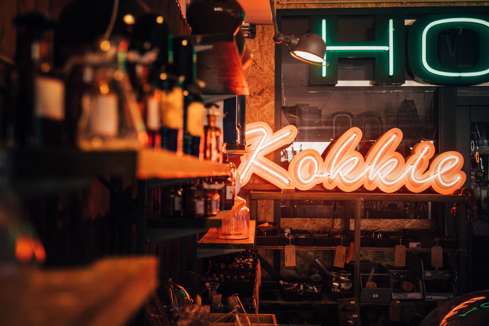 Custom neon verlichting 'Kokkie' samengesteld uit een mix van vintage neon letters in diverse kleuren (blauw, wit, oranje, rood) op een houten wand - maatwerk voorbeeld