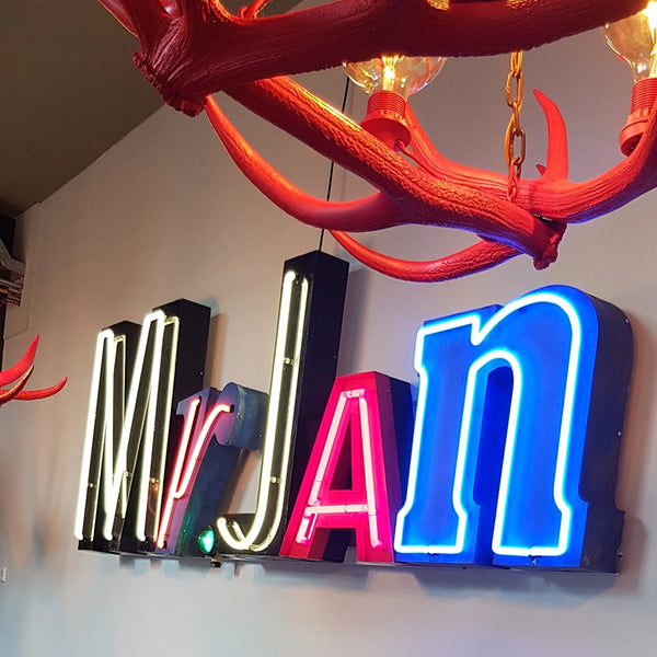 Sfeervol interieur met unieke vintage neon letters 'Mr JAn' aan de muur, gezien achter een rode gewei kroonluchter - horeca inrichting inspiratie